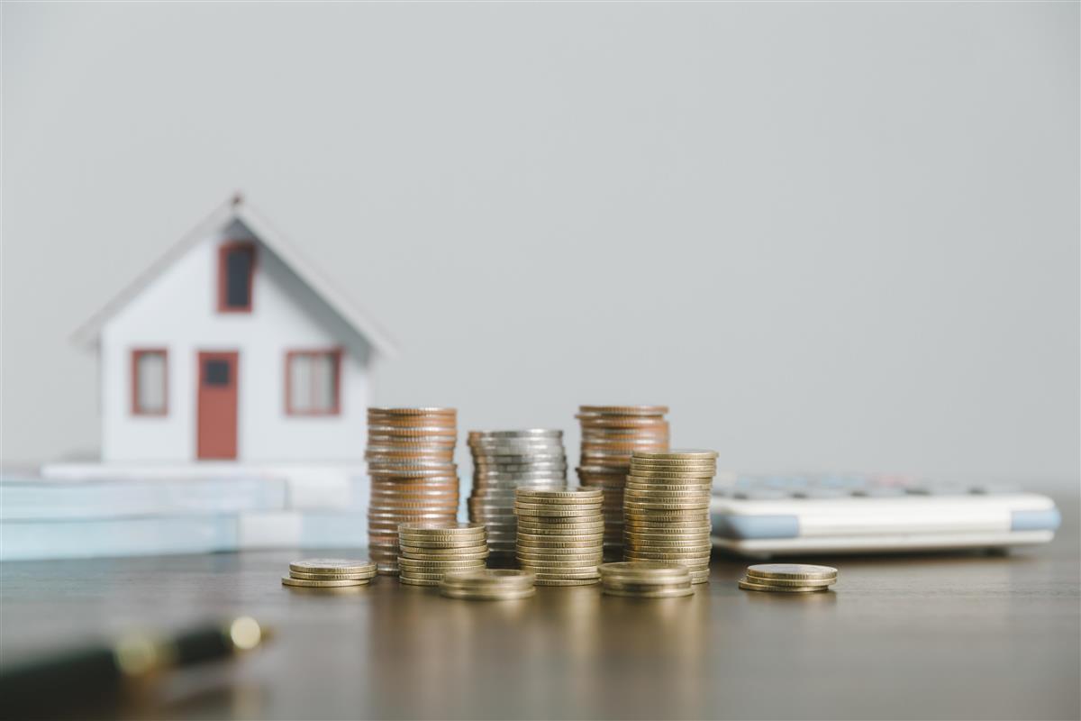 Illustrasjonsfoto for eiendomsskatt lite hus i bakgrunnen med en stabel myntr og kalkulator i fronten - Klikk for stort bilde